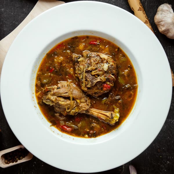 Hearty Indian stew with two large pieces of meat, vegetables, and rich brown sauce in a white bowl.