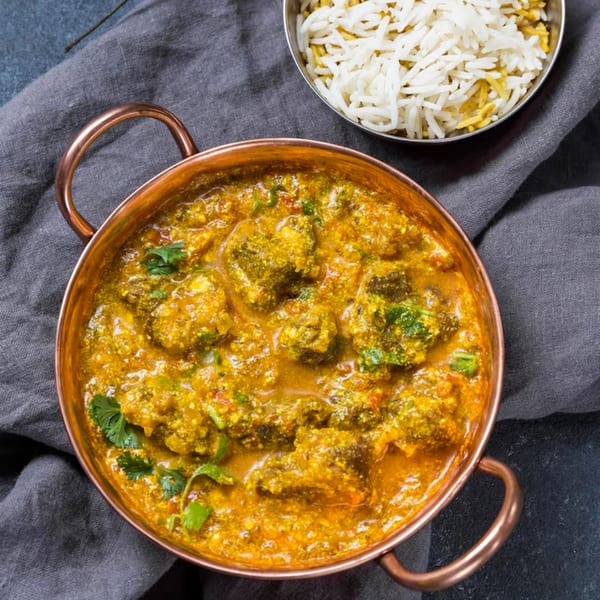 Indian broccoli curry in a copper pot, with a side of basmati rice on a dark cloth.