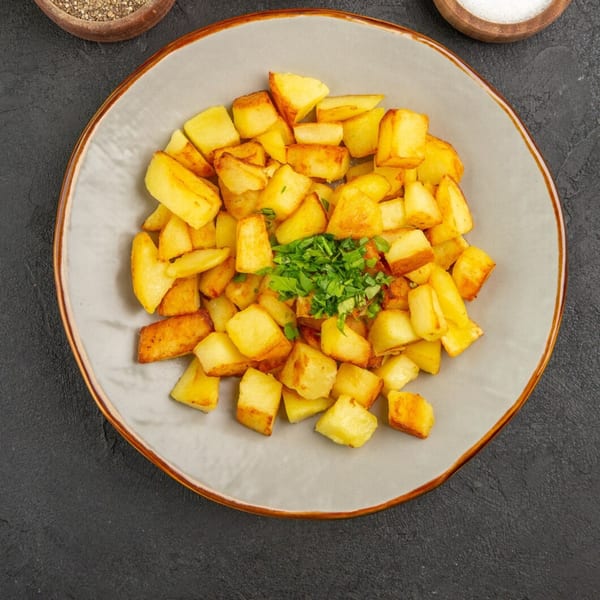 Golden brown fried potato cubes, garnished with fresh green herbs, on a light grey plate.